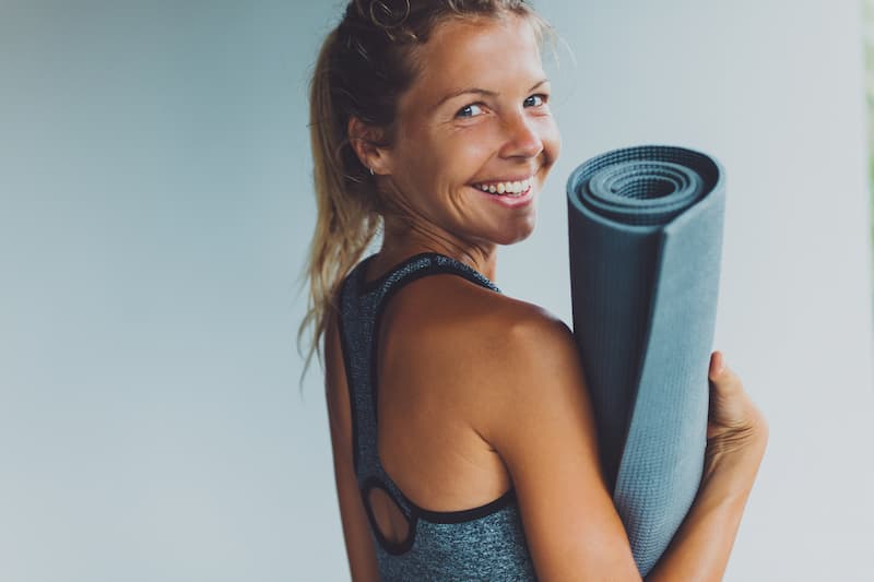 Holding Yoga Mat and Smiling